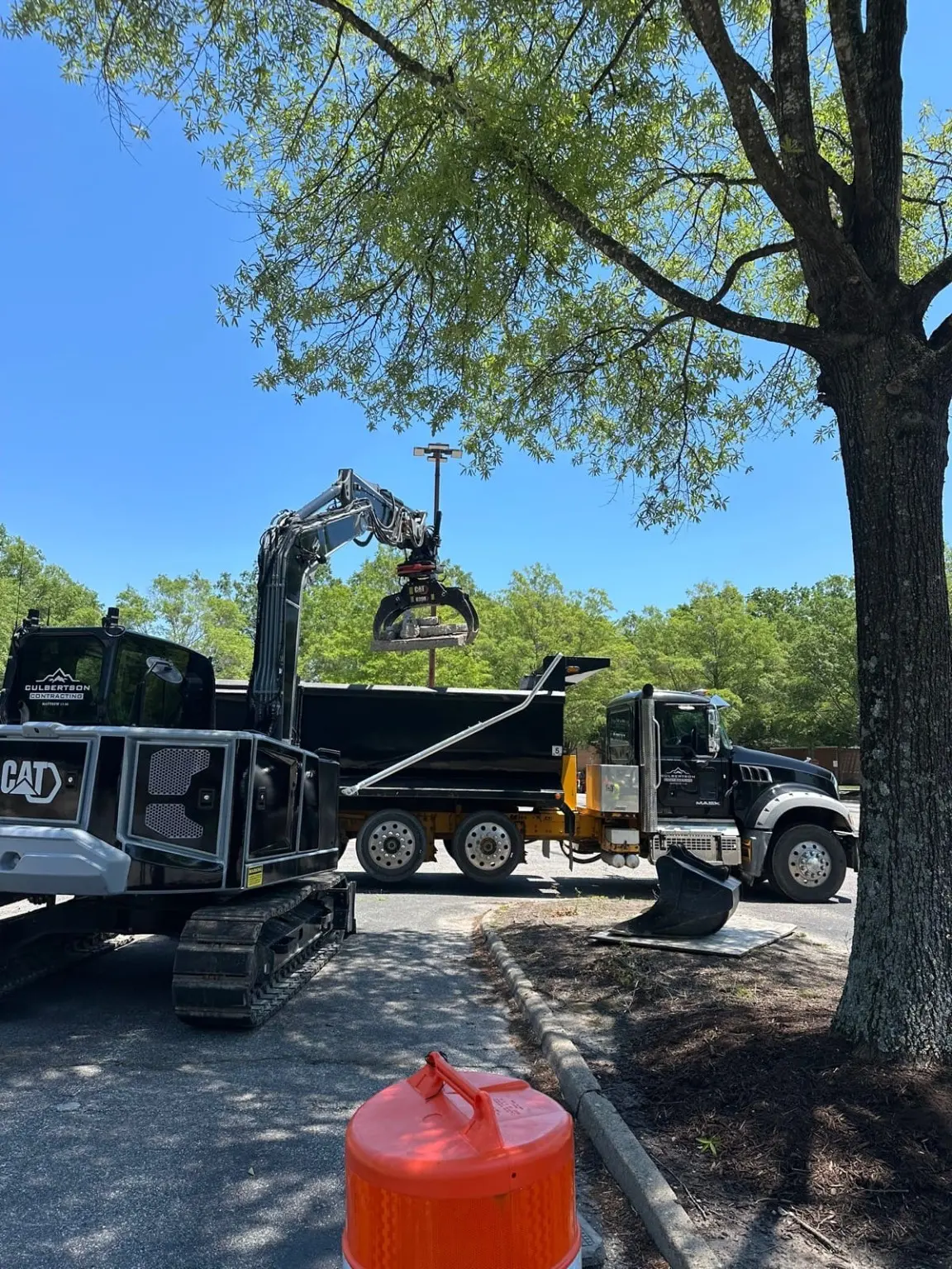Culbertson-branded excavator and dump truck at a work area under a tree.