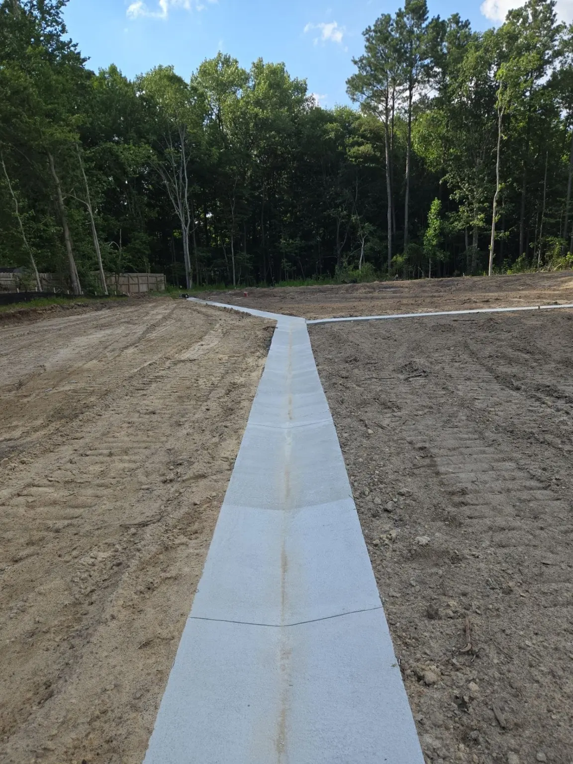 A concrete drainage channel crosses a graded site.