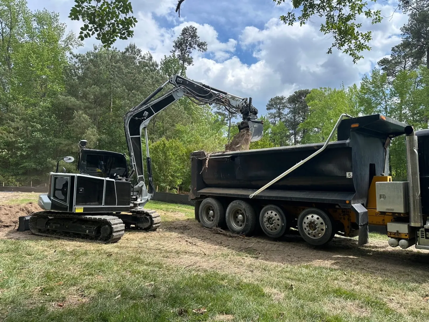 A black-and-silver excavator loads material into a black dump truck.