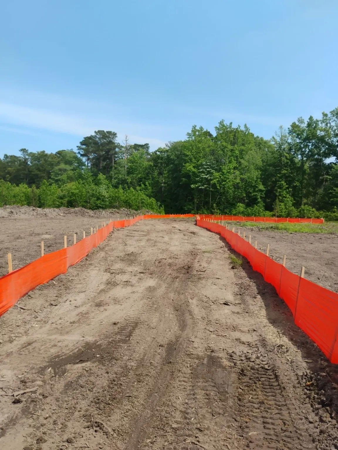 A graded corridor between lines of orange construction fencing.