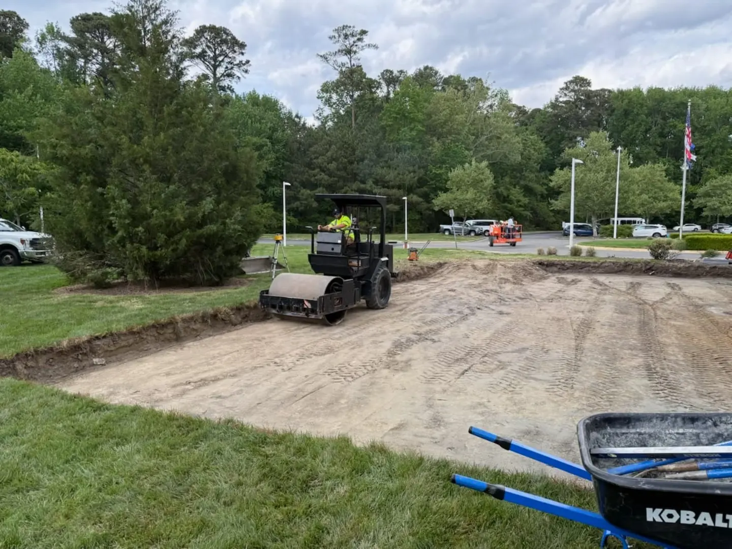 A roller works within a prepared area beside a brick building.