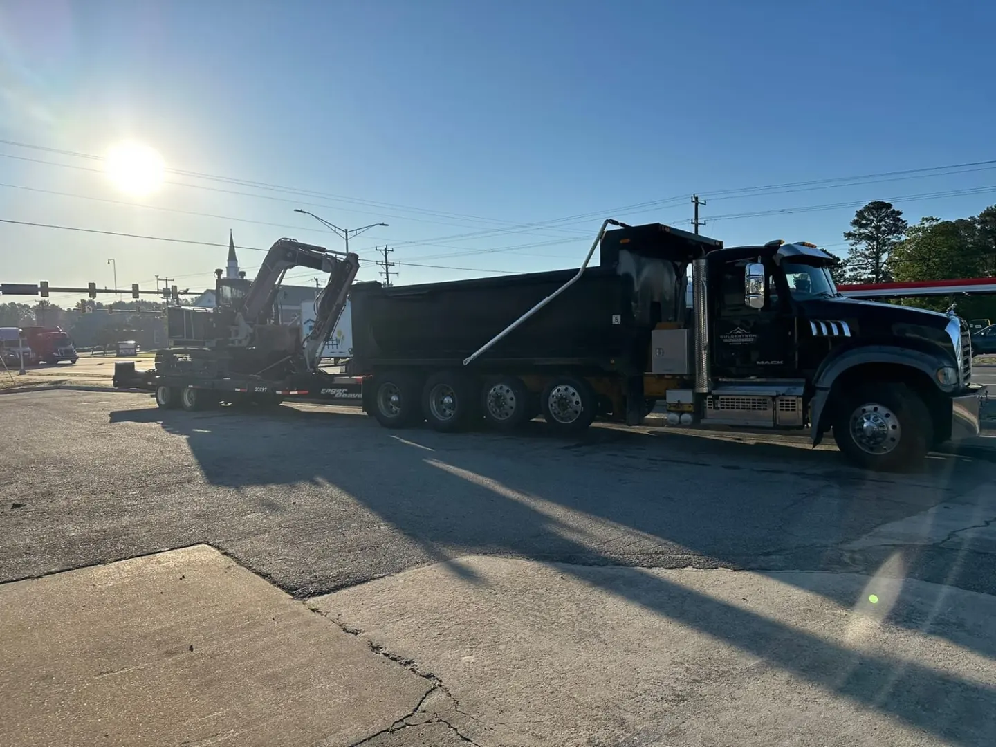 A black dump truck with an excavator on a trailer in low evening light.